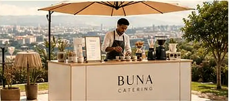 The white BUNA Catering coffee bar on a sunlit terrace under a parasol, with a barista preparing coffee and the city in the background